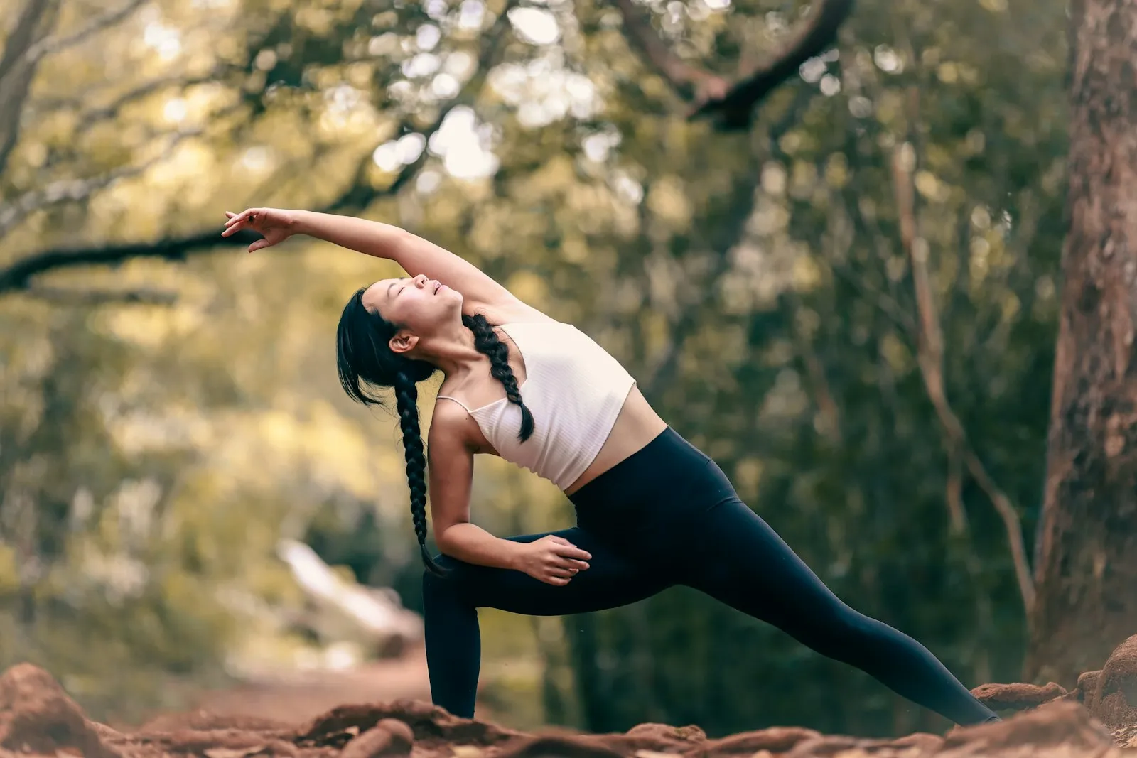 An athlete moving through a mobility stretch on a wooded trail in low evening light